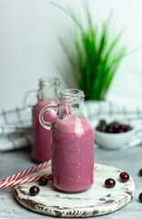 A bottle of cherry smoothies on a white background, cherries in bulk and in a plate. Morning summer breakfast