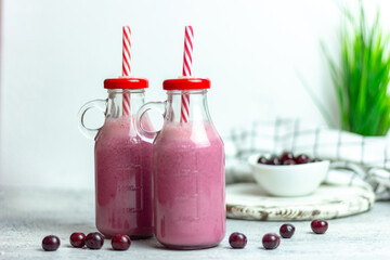 A bottle of cherry smoothies on a white background, cherries in bulk and in a plate. Morning summer breakfast