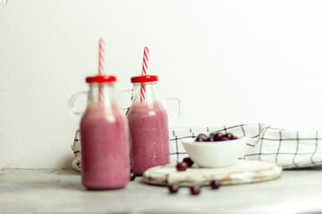 A bottle of cherry smoothies on a white background, cherries in bulk and in a plate. Morning summer breakfast