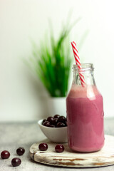 A bottle of cherry smoothies on a white background, cherries in bulk and in a plate. Morning summer breakfast