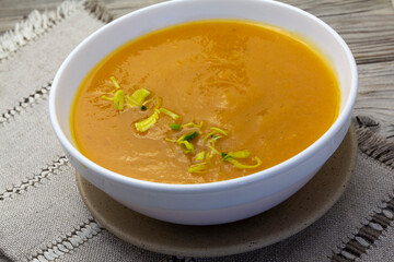 Thick and Creamy Pumpkin Soup in white bowl on wooden rustic background, linen napkin. Healthy eating, horizontal.