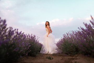beautiful girl in a white wedding dress stands in a lavender field.
