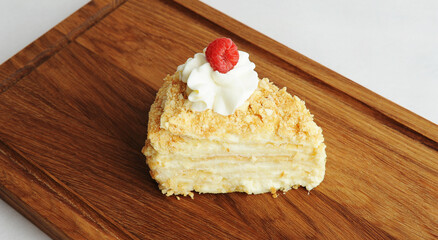 Slice of classic Napoleon cake decorated with cream and fresh raspberries on wooden board