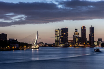 Skyline of Rotterdam early in the morning during blue hour. With no logo's and names, long exposure photo with moving boats. Good view on the Erasmus Bridge in The Netherlands