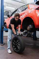 Fototapeta na wymiar Workman in gloves changing tire near car in garage.