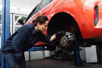 Fototapeta na wymiar Side view of workwoman looking at wheel of car in garage.