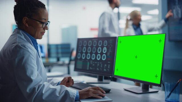 Hospital Research Lab: Black Female Medical Biotechnology Scientist Working on Green Screen Chroma Key Computer with Brain Scan MRI Images. Background: Neuroscientists Have Meeting Analysing MRI Scan