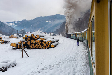 Photo of a narrow gauge steam locomotive, steaming through the winter landscape. Photo was shot from the train while moving. Photography of a touristic narrow gauge train 