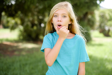 Fototapeta premium Caucasian little kid girl wearing blue T-shirt standing outdoors Looking fascinated with disbelief, surprise and amazed expression with hands on chin