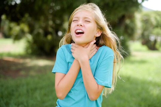Caucasian little kid girl wearing blue T-shirt standing outdoors shouting suffocate because painful strangle. Health problem. Asphyxiate and suicide concept.
