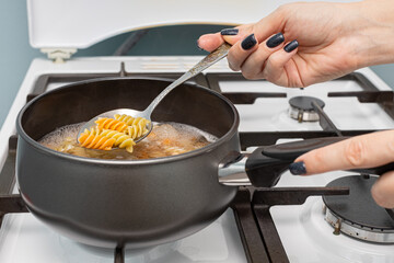 a woman's hand takes a spoonful of pasta out of the pan