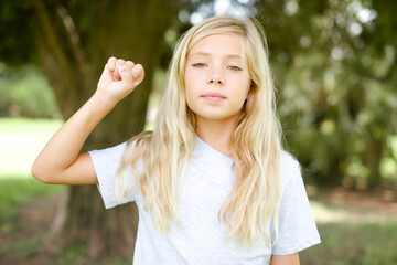 Caucasian little kid girl wearing white T-shirt standing outdoors pointing up with fingers number ten in Chinese sign language Shi