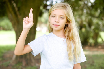 Caucasian little kid girl wearing white T-shirt standing outdoors pointing up with fingers number ten in Chinese sign language Shi