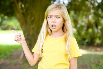 Emotive beautiful Caucasian little kid girl wearing yellow T-shirt keeps jaw dropped from shock demonstrates amazing promo points right on blank space demonstrates big shopping sale. Advertisement