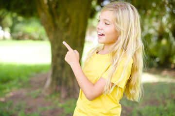 beautiful Caucasian little kid girl wearing yellow T-shirt standing outdoors glad cheery demonstrating copy space look novelty