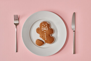 Homemade gingerbread Christmas cookie in the form of a man on a white plate on pink background