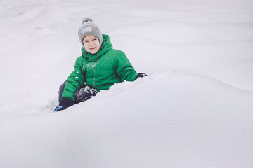 Fototapeta na wymiar Happy boy sitting on snow in winter park
