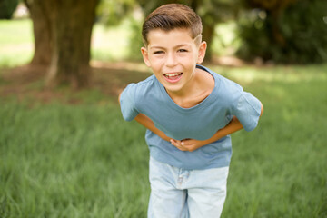 beautiful Caucasian little kid boy wearing blue T-shirt standing outdoors smiling and laughing hard out loud because funny crazy joke with hands on body. - obrazy, fototapety, plakaty