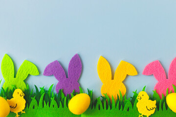Obraz na płótnie Canvas Colorful Easter bunnies, eggs and chickens in grass on blue background, top view with space for text. Happy Easter! Pink and yellow artificial eggs and bunnies decor with green grass