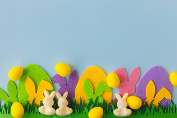 Happy Easter! Colorful Easter bunnies, eggs in grass on blue background, top view with space for text. Pink and yellow artificial eggs and bunnies decor with green grass