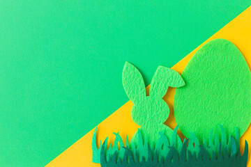 Green Easter egg and bunny in grass on green and yellow background, flat lay with space for text....