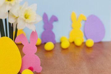 Colorful Easter bunnies, eggs and daffodils bouquet on table against blue background with space for text. Happy Easter! Purple, yellow, pink artificial decor and spring flowers. Easter hunt