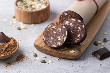 Chocolate sausage with oatmeal and seeds on gray textured background. Delicious healthy vegan dessert