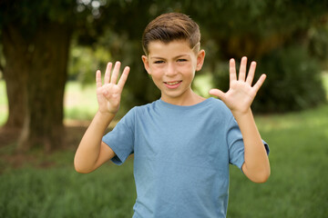 beautiful Caucasian little kid boy wearing blue T-shirt standing outdoors showing and pointing up with fingers number nine while smiling confident and happy.