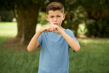 beautiful Caucasian little kid boy wearing blue T-shirt standing outdoors Has rejection angry expression crossing fingers doing negative sign.
