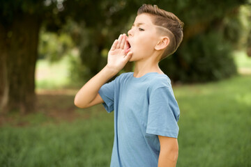 Fototapeta premium Caucasian little kid boy wearing blue T-shirt standing outdoor shouting and screaming loud to side with hand on mouth. Communication concept.