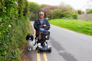 Disabled man on mobility scooter with his spaniel dog by his side enjoying the freedom and independence the vehicle allows him to get out and about.