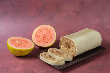 Sliced bolo de rolo on a brown plate, next to a guava.