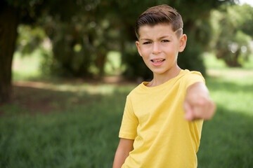 Excited positive Caucasian little kid boy wearing yellow T-shirt standing outdoors points index finger directly at you, sees something very funny. Wow, amazing