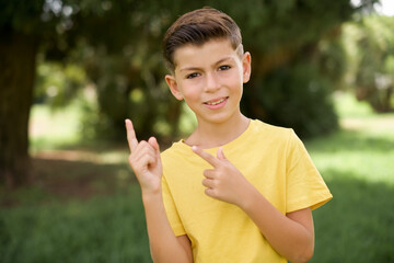 Caucasian little kid boy wearing yellow T-shirt standing outdoors points at copy space indicates for advertising gives right direction