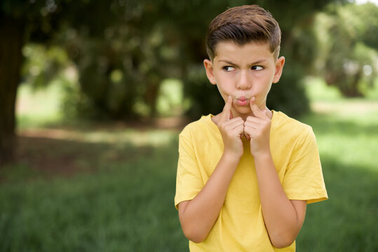 Caucasian little kid boy wearing yellow T-shirt standing outdoors crosses eyes and makes fish lips funny grimace