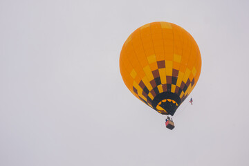 Colorful orange hot air balloon flying against grey sky at Winter aerostat festival, snow falling....