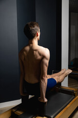 Sporty man doing exercises on pilates reformer training machine. Working out wearing sportswear, gym.