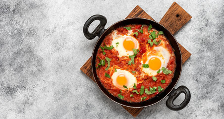 Shakshuka in a frying pan on a gray rustic background. Poached eggs in a spicy tomato pepper sauce. Typical Jewish or Arabic food. Top view, flat lay. Banner