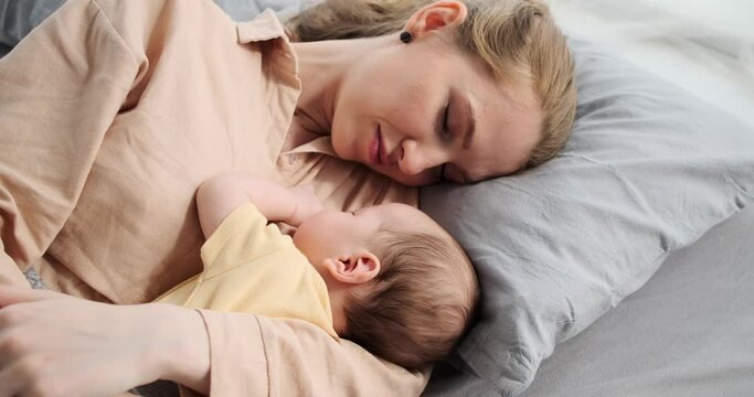 Young mother and her baby son sleeping on bed in bedroom at home