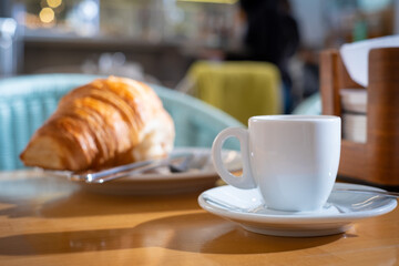 Breakfast with a a cup of white coffee and croissant in background