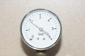 Manometer instrument with white dial on wall of brown ceramic tiles