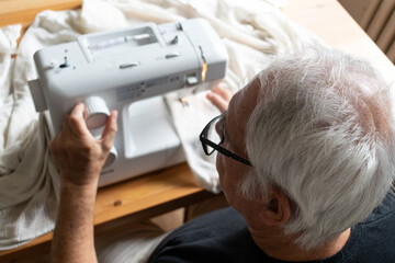 old male man senior sit next at table at home work, sewing machine enjoy