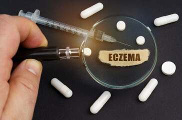 A man looks through a magnifying glass at pills, a syringe and a piece of paper with the inscription - ECZEMA