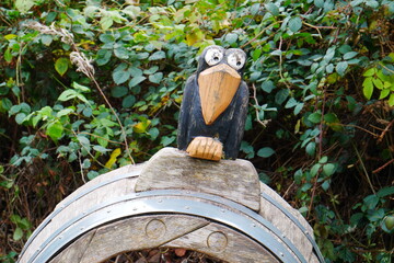 a funny looking wooden raven sits on an old wooden barrel