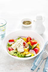 Fresh summer vegetable salad with lettuce, tomato, cucumber, bell pepper, onion and feta cheese, dressed with olive oil