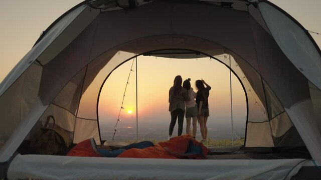 group of young Asian friends standing and taking pictures and relaxing in front of a tent during a summer camping vacation in the evening when the sunset.concept of freedom, leisure, travel, adventure