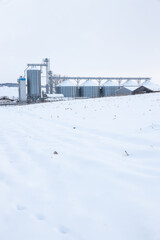 Silos in a cold winter day and stubble corn field covered with snow in foreground