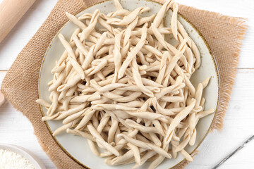 Whole grain wheat raw apulian pasta called Pizzarieddi or maccaruni on a ceramic plate on white wooden table. Fresh maccheroni typical dish of Puglia, Salento Italy. Italian homemade pasta background
