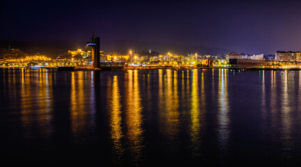 Skyline cityscape of Almeria at twilight from the lighthouse, Andalusia, Spain. Lights of metropolis shining in the seawater. Panorama.