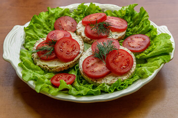 dietetic crispbreads with cream cheese and tomato slices on lettuce leaves on a plate, healthy...